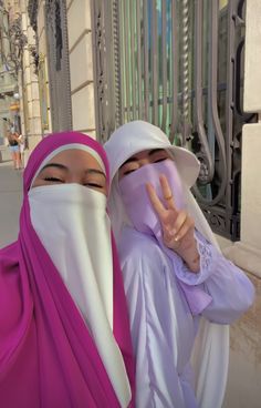 two women dressed in hijabs making the peace sign