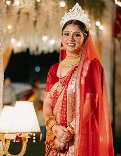 a woman wearing a red and gold bridal outfit standing in front of a chandelier