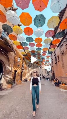 a woman standing in the middle of an alley with many umbrellas overhead