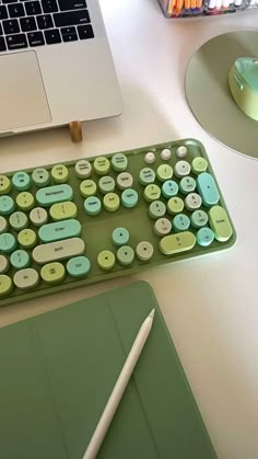 a green keyboard sitting on top of a desk next to a laptop and a pen