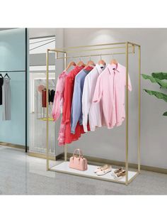 a clothing rack with clothes and shoes on it in a store or office space, next to a plant