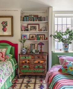 a bedroom with two beds and a dresser in the corner next to a window filled with books