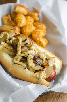 a hot dog on a bun with toppings next to tater tots