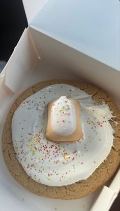 a cookie with white icing and sprinkles in a box