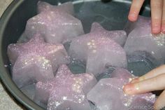 two hands reaching for some ice cubes in a pan filled with water and sugar