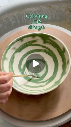 a person is holding a stick in a bowl with green swirls on the inside