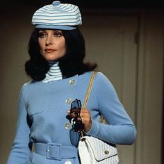 a woman in a blue coat and hat holding a white purse