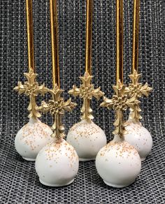 four white and gold decorated christmas balls on a table with golden candlesticks in the background