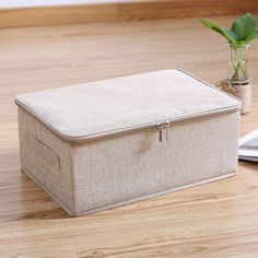 a beige storage box sitting on top of a wooden floor next to a potted plant