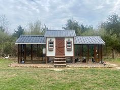 a small house with a metal roof in the middle of a grassy area next to trees