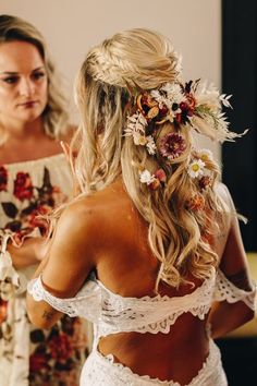 a woman with flowers in her hair standing next to another woman wearing a white dress