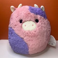 a pink and purple stuffed animal sitting on top of a white table next to an orange wall