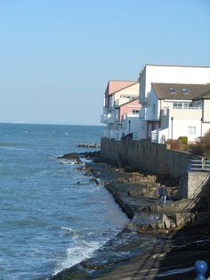 people are walking on the beach near some houses and water in front of them,