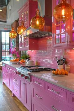 a kitchen with pink cabinets and lights hanging above the stove top, along with oranges on the counter