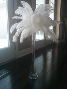 a tall glass vase filled with white feathers on top of a wooden floor next to a door