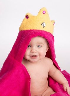 a baby wrapped in a pink towel with a crown on it's head and smiling