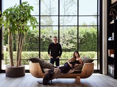 two people and a dog sitting on a couch in front of a large glass window