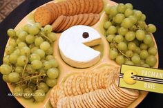 a plate with grapes, crackers and cheese on it that says pacman's bite