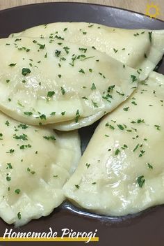 three ravioli with parsley on top in a black plate sitting on a wooden table