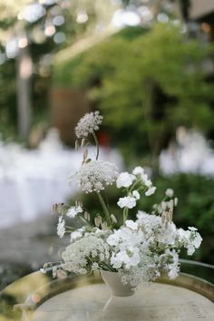 white flowers in a vase sitting on top of an old barrel table outside at a wedding reception