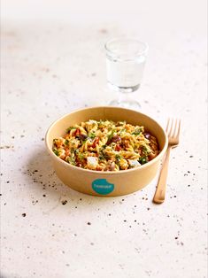 a bowl of food next to a glass of water and a fork on a table