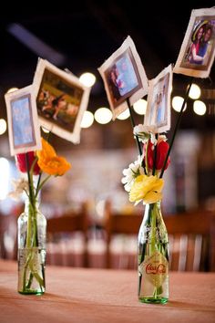 three vases with flowers in them sitting on a table next to framed pictures hanging from the ceiling