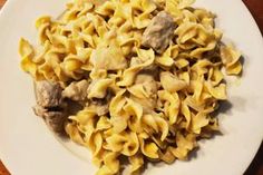 a white plate topped with pasta and meat on top of a wooden table next to a fork