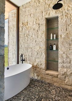 a bath tub sitting next to a stone wall with shelves on the side of it