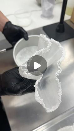 a person in black gloves is making something out of white paper on a metal table