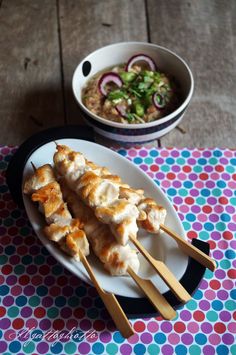 chicken skewers on a plate next to a bowl of soup and chopsticks