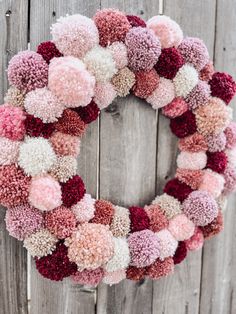 a wreath with pom - poms hanging on a wooden fence