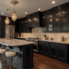 a large kitchen with black cabinets and marble counter tops, two stools at the island