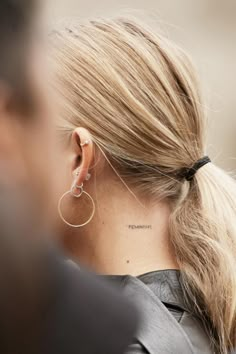 a woman with her hair in a ponytail has a small tattoo on her left ear