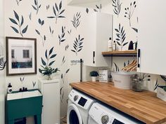 a washer and dryer in a small room next to a wall with leaves painted on it