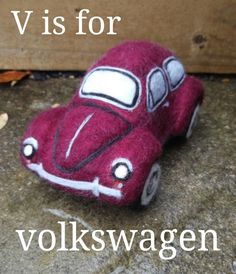 a red toy car sitting on top of a cement floor next to a wooden wall