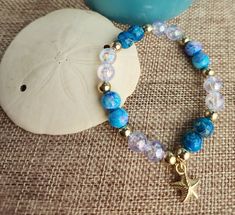 Elegant 7-inch bracelet made to fit most adult women.  Delicate golden starfish charm hangs from turquoise blue and iridescent bracelet. Gold Ocean-inspired Starfish Bracelets, Adjustable Blue Bracelets With Starfish Charm, Adjustable Blue Starfish Jewelry, Adjustable Gold Charm Bracelet With Starfish Charm, Blue Bracelet With Starfish Charm And Round Beads, Blue Bracelets With Starfish Charm And Round Beads, Adjustable Turquoise Beaded Charm Bracelet, Adjustable Starfish Bracelet With Lobster Clasp, Adjustable Blue Jewelry With Starfish Charm