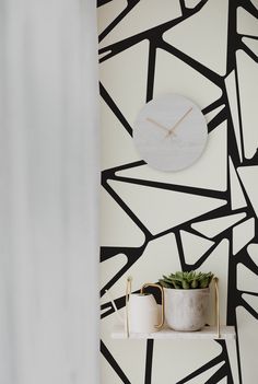 a white clock mounted to the side of a wall next to a potted plant