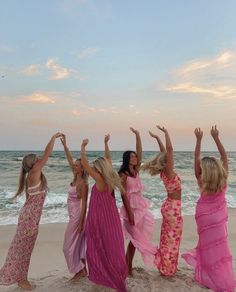 four women in long dresses standing on the beach with their hands up and arms raised