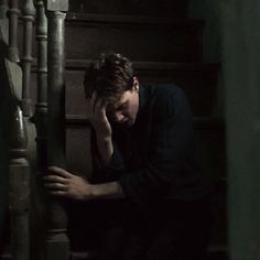 a young man sitting on the stairs with his head in his hands and looking down