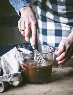 a person mixing something in a bowl with a whisk and a cloth on the table