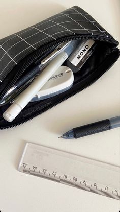 a pencil, ruler and pen sitting on top of a white table next to a black wallet