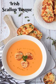 there is a bowl of soup with shrimp on the side and bread in the background