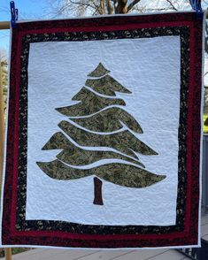 a quilted christmas tree hanging on a clothesline with trees in the back ground