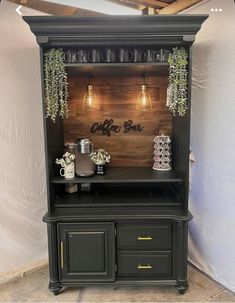 a black hutch with plants and coffee mugs on top