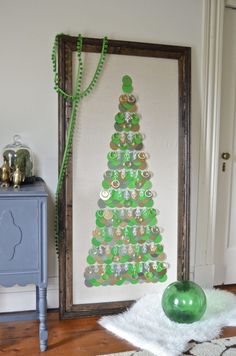 a christmas tree made out of green buttons on a white wall next to a wooden frame