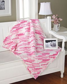 a pink and white crocheted blanket sitting on top of a bed next to a window