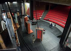 an empty theatre with red seats and people standing around the stage looking down at them