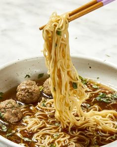 someone is holding chopsticks over noodles in a bowl with meatballs and sauce