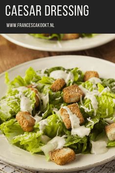 two white plates topped with lettuce and croutons covered in ranch dressing