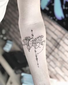 a person with a tattoo on their arm holding a small world map and an arrow